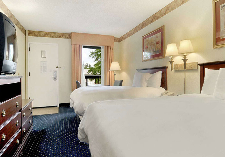 two double beds across from dresser with TV, and table with two chairs at Baymont by Wyndham Tallahassee